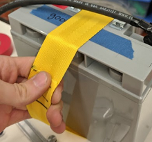 Un ejemplo que muestra una correa de nylon de 2" de ancho, envuelta alrededor de la batería y cosida en un bucle.